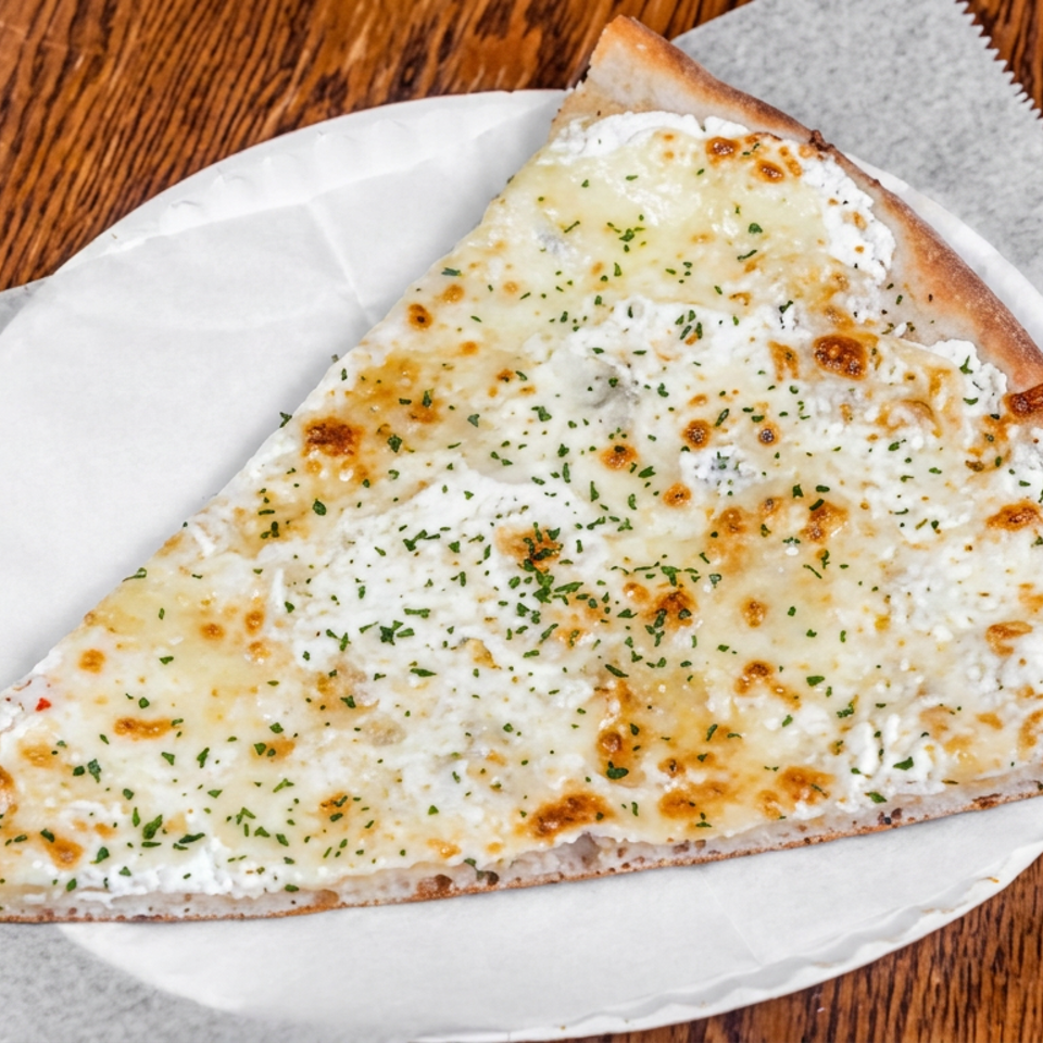 Large slice of white cheese pizza sprinkled with herbs on a paper-lined plate atop a wooden table.
